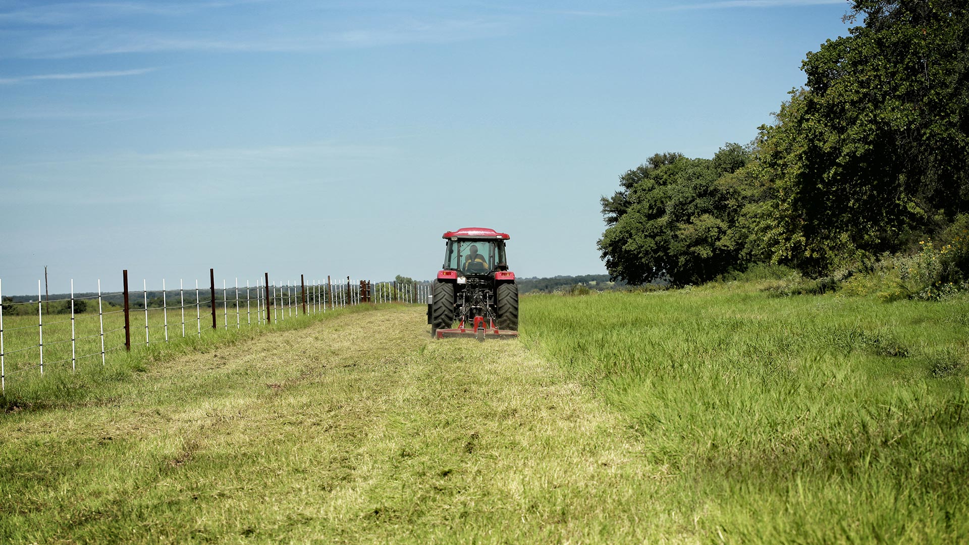 A bush hogger driving away by a fence in Moro, Illinois.