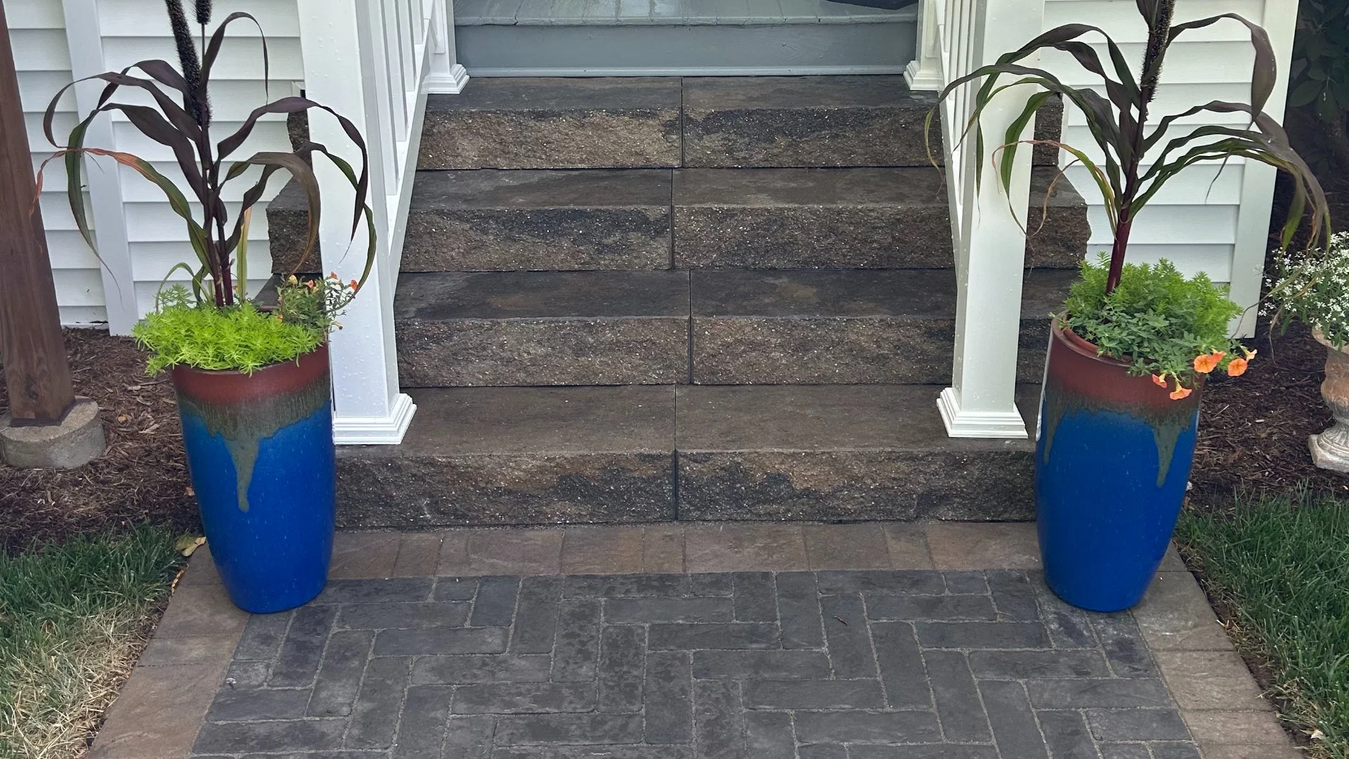 Close-up of colorful planters on either side of textured stone steps leading to a home's entrance