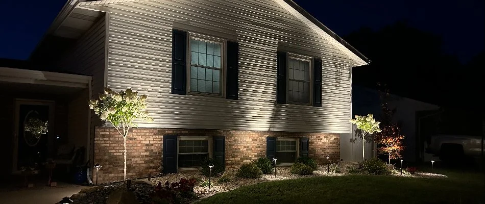 Charming home exterior lit at night, highlighting landscaped garden and unique architectural details.