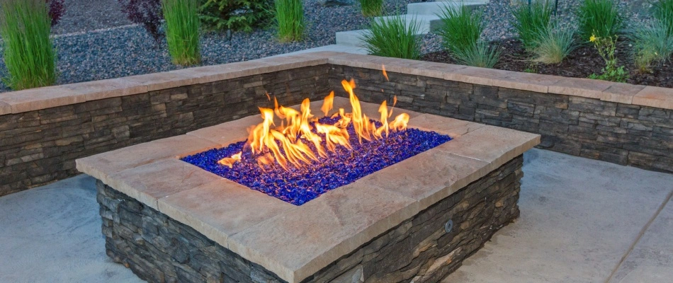 Gas burning fire pit with blue glass rocks in patio retaining wall area near Holiday Shores, IL.