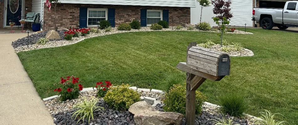 Green lawn and landscape in Madison County, IL, with plants, rocks, and mailbox.