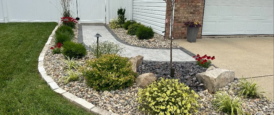 Side view of a house with a landscaped yard, featuring flower beds, rocks, and a young tree.